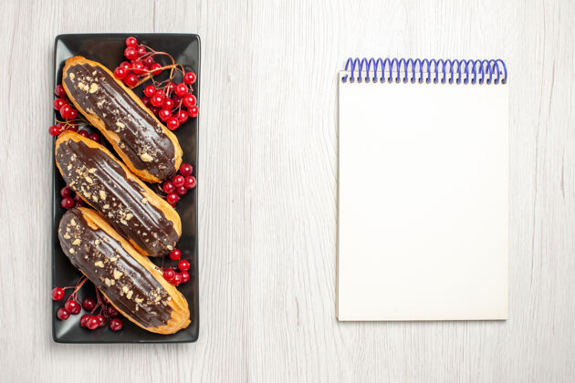 右边在左边的黑色矩形板上俯视巧克力和醋栗 在白色木质地面的右边俯视笔记本手镯左边礼品
