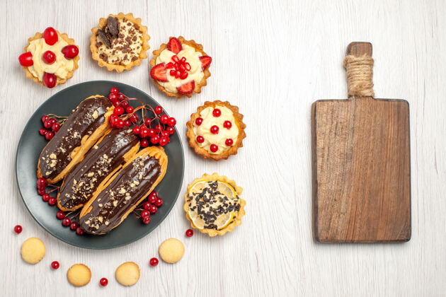 木板俯瞰图：灰色盘子上的巧克力沙拉和葡萄干 周围是馅饼和饼干 白色木桌上有一个砧板馅饼器械一餐