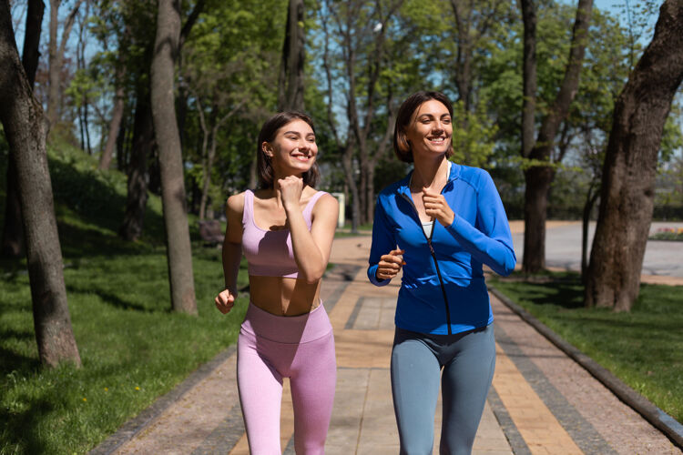 健康两位积极快乐的女性朋友一起在公园小径跑步慢跑笑笑活跃女人大笑