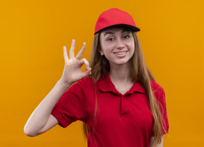 标志微笑着的年轻送货女孩穿着红色制服 在孤立的橙色空间上做着“ok”的手势制服年轻好