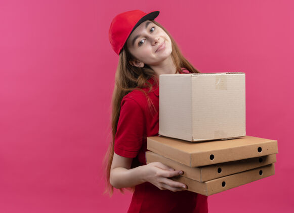 空格高兴的年轻送货女孩在红色制服举行的箱子和包裹上孤立的粉红色空间与复制空间请盒子复印件