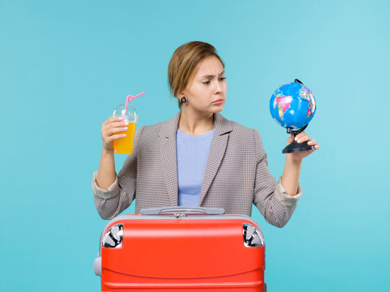 旅行前景度假中的女性手持新鲜果汁和地球仪在蓝色背景海上度假旅行人卖方前面