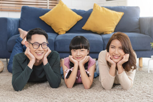 男性放松亚裔家庭躺在家里客厅的地毯上 开心地微笑着女孩放松欢乐