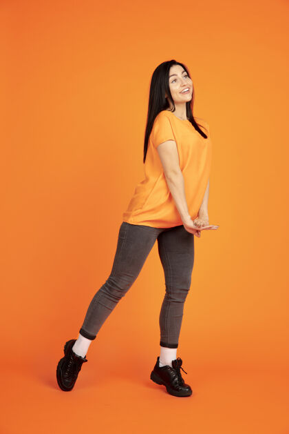 女性橙色工作室背景上的白种人年轻女子肖像穿着衬衫的漂亮黑发女性模特人类情感的概念 面部表情 销售 广告广告空间跳舞 大笑半身帅哥员工