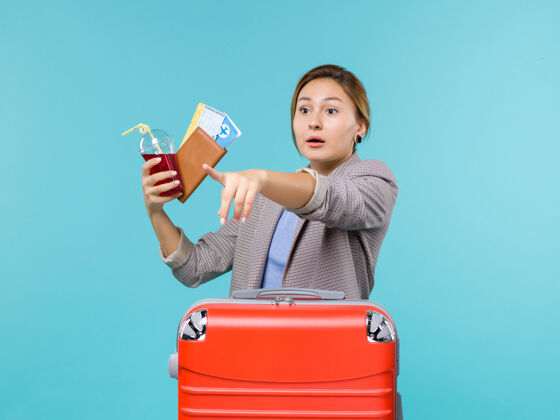 举行前视图：度假中的女性手持果汁和浅蓝色背景的机票旅行度假海上飞机微笑票旅行