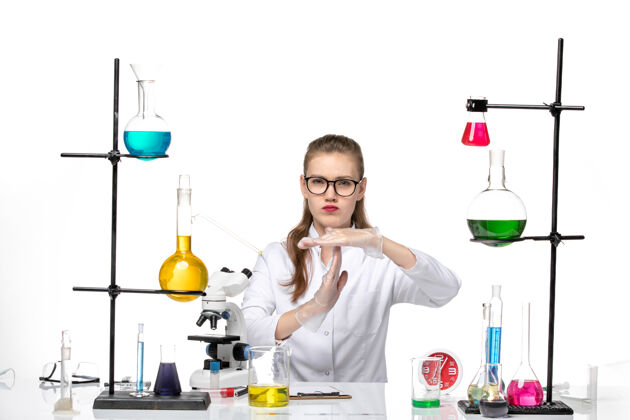 烧杯前视图穿着白色医疗服的女医生坐在白色背景病毒健康病毒大流行化学的解决方案实验室研究化学