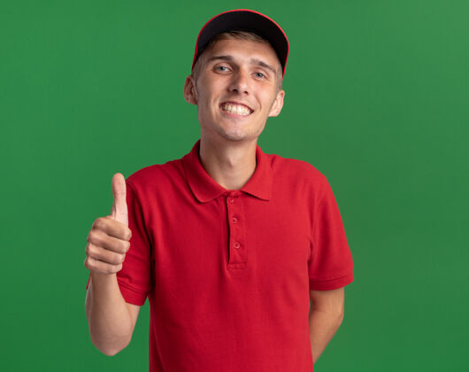 向上微笑着的年轻金发送货员竖起大拇指站在绿色交货绿色男孩
