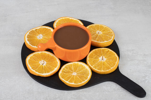 热一杯咖啡和一盘橙子片放在深色的木板上切片食物一餐