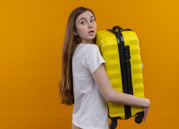 印象令人印象深刻的年轻旅行家女孩拿着手提箱 看着身后孤立的橙色空间和复印空间空间橙色持有