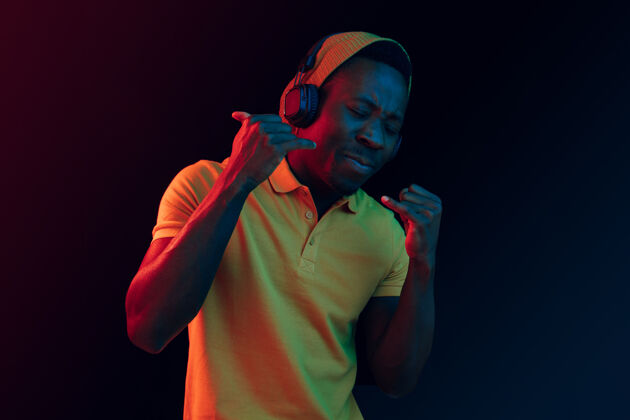 牙买加年轻帅气快乐的时髦男人在霓虹灯下用耳机在黑工作室听音乐迪斯科舞厅 夜总会 嘻哈风格 积极的情绪 面部表情 舞蹈概念肖像耳机脸