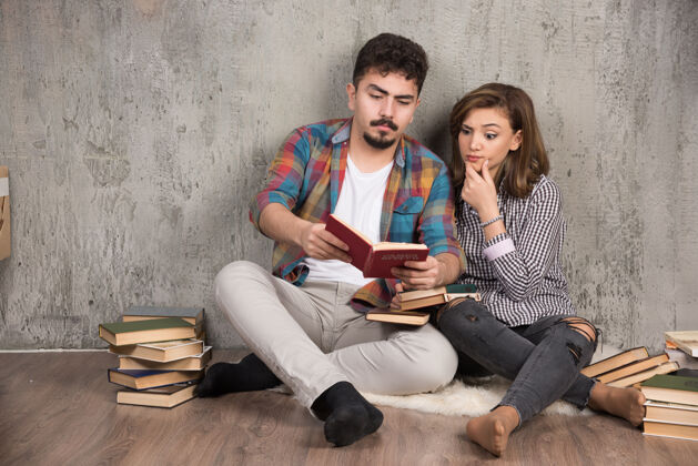 坐着可爱的夫妇坐在地板上读一本有趣的书文学乐趣举行