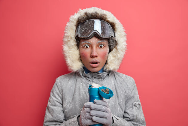 惊艳冬天的概念惊讶的年轻民族妇女红脸穿暖和的夹克衫和风帽花在最喜欢的业余爱好滑雪或滑雪板冬天冰冻粉色