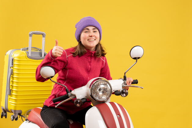人正面图：骑着轻便摩托车的快乐的年轻女子竖起大拇指人人给予