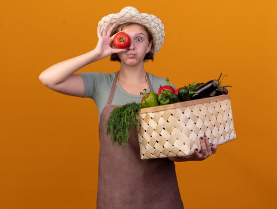 篮子年轻的斯拉夫女园丁戴着园艺帽 手里拿着菜篮子和西红柿 眼前一片橘色前面年轻蔬菜