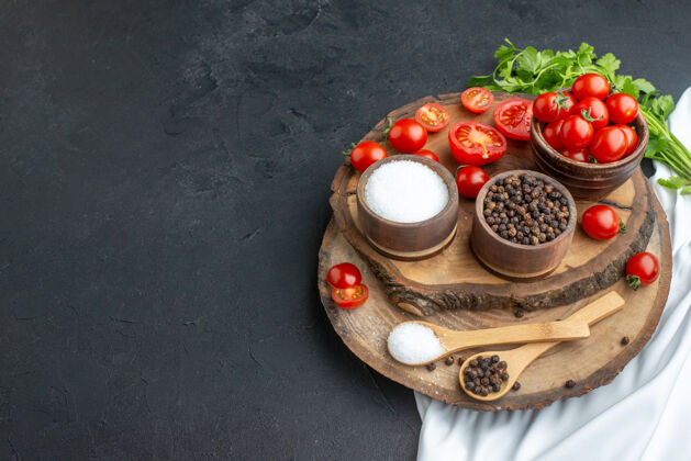 容器新鲜西红柿和香料的顶视图在黑色表面的左侧木板上的碗 汤匙里香料食物碗