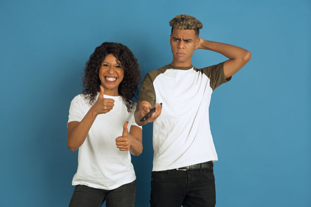 选择年轻感性的非裔美国人男女在蓝色背景上摆姿势美丽的情侣人类情感的概念 面部表情 关系 广告一起看电视 她最喜欢的频道女孩人化妆