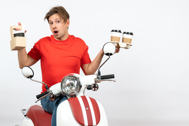 摩托车穿着红色制服的年轻人坐在滑板车上 在黄色的墙上拿着命令快乐自行车年轻
