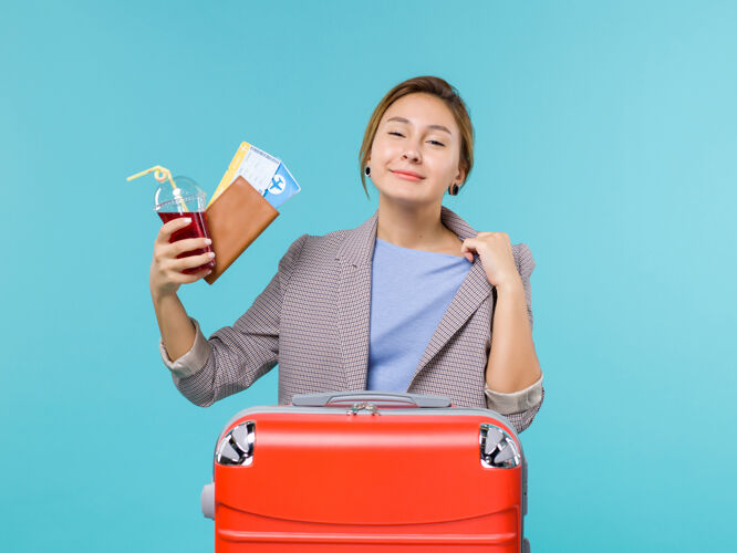 微笑正面图：度假中的女性拿着果汁和蓝色背景的机票旅行度假海上飞机救济看法旅行