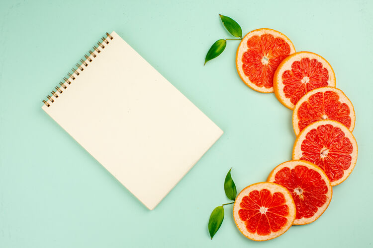 健康美味的新鲜葡萄柚 多汁的水果切片 浅蓝色表面上有记事本纸张食品节日