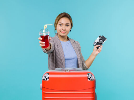 风景前视图：度假中的女性拿着果汁和相机在淡蓝色的背景上旅行度假旅行海上飞机微笑航行人