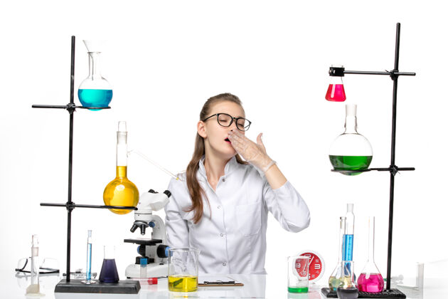 实验室前视图穿着白色医疗服的女医生坐在桌子前 在白色地板上打呵欠 科维德化学病毒大流行医学哈欠坐着