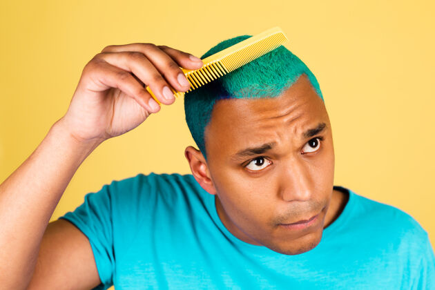 成人黑人非洲男人在随意的黄色墙壁上刷蓝色亮丽的头发 美容院的概念脸发型男人