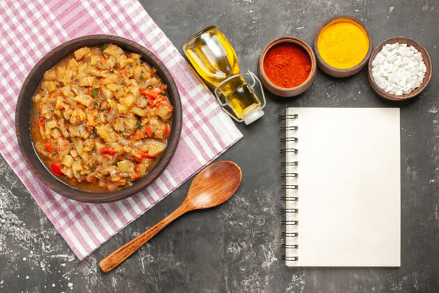 碗顶视图烤茄子沙拉在碗里 油 木勺 不同的香料和笔记本在黑暗的表面不同茄子沙拉勺子