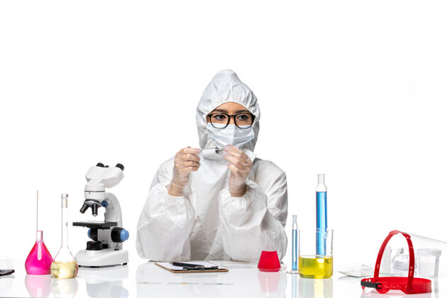 西装正面图身着特殊防护服的女化学家拿着针剂在浅白的办公桌上化学冠状病毒大流行病毒桌子男人