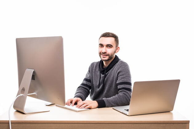 电脑自信的年轻企业家坐在桌边 拿着笔记本电脑和个人电脑 看着隔离在白色屏幕上的相机桌子一个笔记本电脑