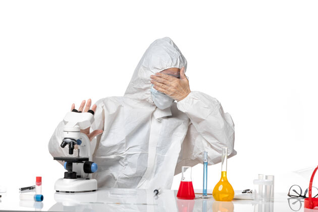 男性正面图女医生穿着防护服戴着口罩由于害怕用显微镜观察白色背景病毒大流行飞溅的病毒专业人正面