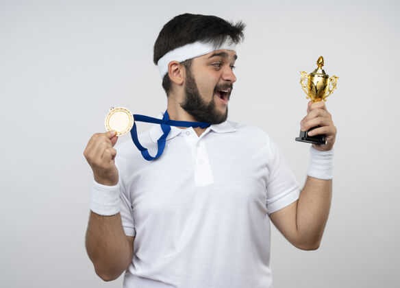 个人惊讶的年轻人戴着头带和腕带拿着冠军杯戴着和拿着奖牌看奖杯男子惊喜