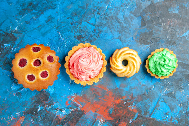 鲜花水平排树莓纸杯蛋糕的俯视图 蓝色表面上的小馅饼和饼干鲜花玫瑰爱情