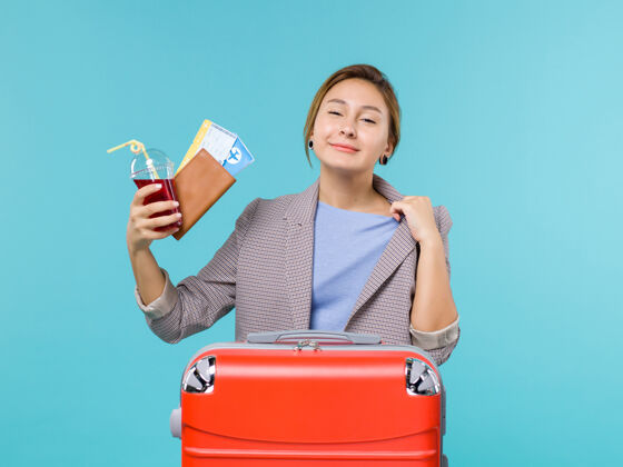 微笑正面图：度假中的女性拿着果汁和蓝色背景的机票旅行度假海上飞机救济看法旅行