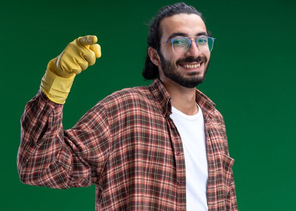 人面带微笑的年轻帅气的保洁员穿着t恤 戴着手套点在前面隔离在绿色的墙上微笑姿势感觉