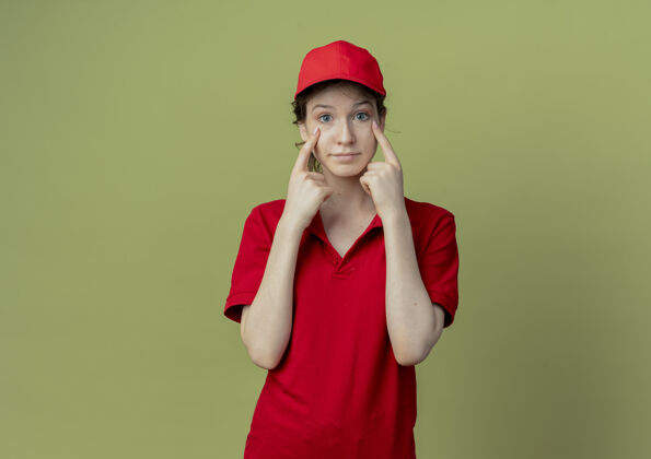 漂亮令人印象深刻的年轻漂亮的送货女孩在红色制服和帽子把手指下的眼睛隔离在橄榄绿的背景与复制空间制服手指交货