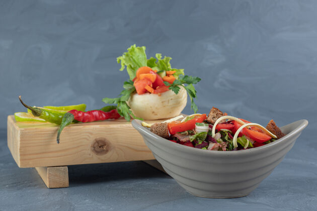 柠檬灰色沙拉碗旁边的一捆蔬菜放在大理石桌上的木板上美味美味胡椒