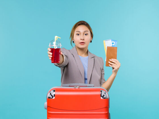 航行正面图：度假中的女性手持新鲜的樱桃汁和蓝色背景上的机票旅行旅行飞机旅行旅行举行前面女人