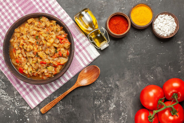 深色顶视图烤茄子沙拉在碗油 木勺和西红柿在黑暗的表面一餐勺子蔬菜