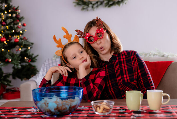 桌子快乐的母亲和坐在餐桌旁的女儿在家里享受圣诞节时光快乐时间女儿