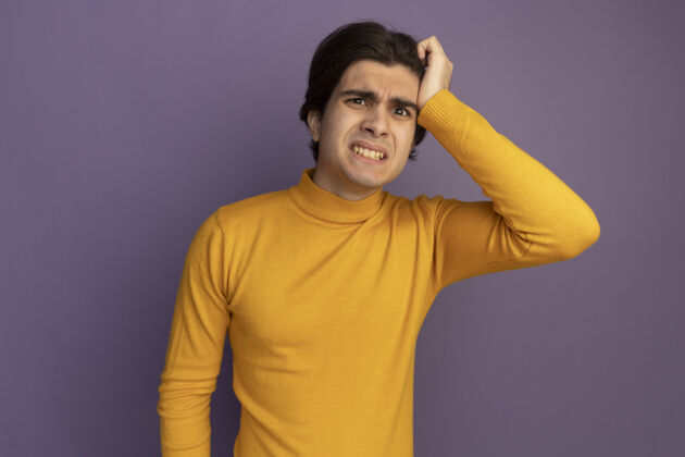 人关心的年轻帅哥穿着黄色高领毛衣把手放在太阳穴隔离在紫色的墙上高领毛衣穿着手