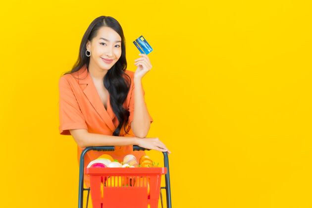 泰国菜肖像美丽的亚洲年轻女子微笑着从黄色超市购物篮杂货店休闲产品