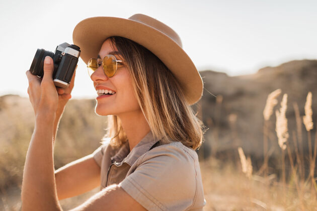 女人穿着卡其色长裙的美丽时尚的年轻女子在沙漠中旅行 在非洲旅行 戴着帽子在老式相机上拍照模特美丽休闲