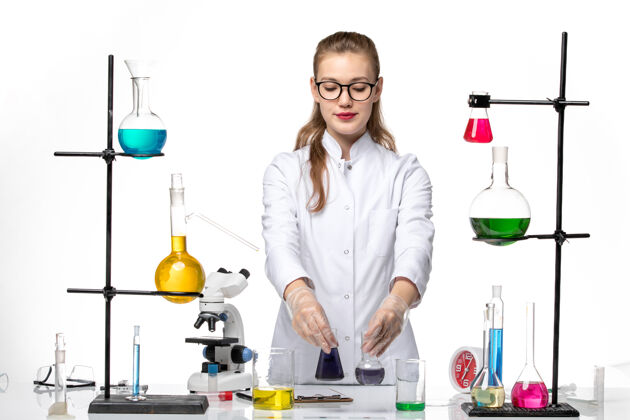 医学前视图穿着医疗服的女化学家在白色办公桌上用不同的解决方案化学大流行的冠状病毒视野人办公桌