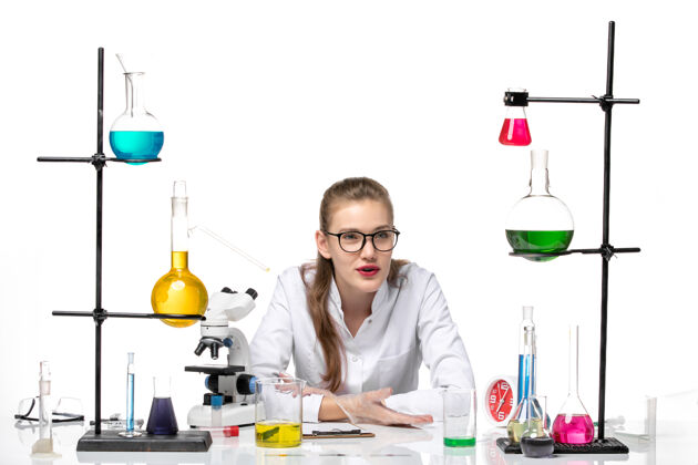坐姿前视图穿着医疗服的女化学家坐在白色背景上 用不同的解决方案化学大流行健康covid健康正面人