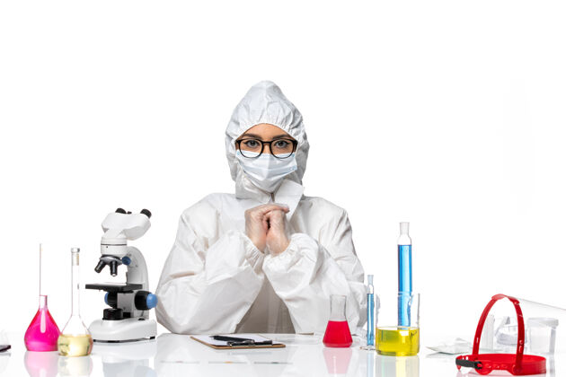 健康前视图穿着特殊防护服的女化学家坐在白色化学背景上的解决方案-病毒大流行专业坐姿口罩