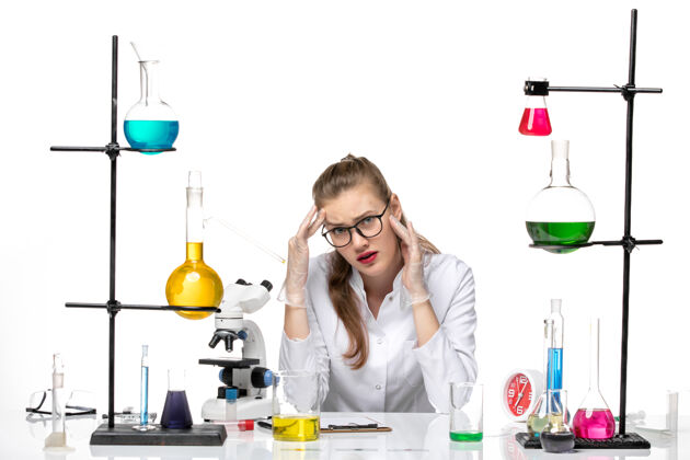 前面前视图穿着医疗服的女化学家坐在白色办公桌上 拿着解决方案大流行性化学冠状病毒女化学家白人专业
