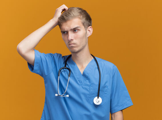 人困惑的年轻男医生穿着医生制服 听诊器在橙色的墙上划破了头人年轻头