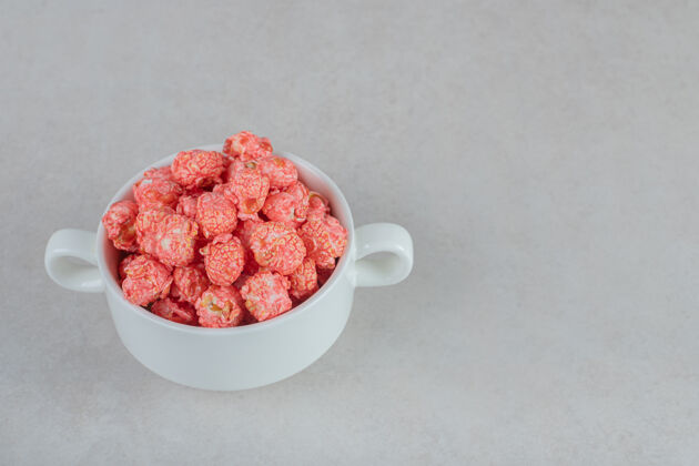 碗有把手的碗 在大理石桌上放着红色涂层的爆米花玉米垃圾食品爆米花