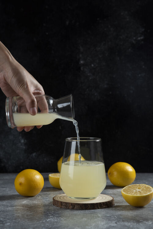 自制一只手把柠檬汁倒进杯子里玻璃柠檬水罐子