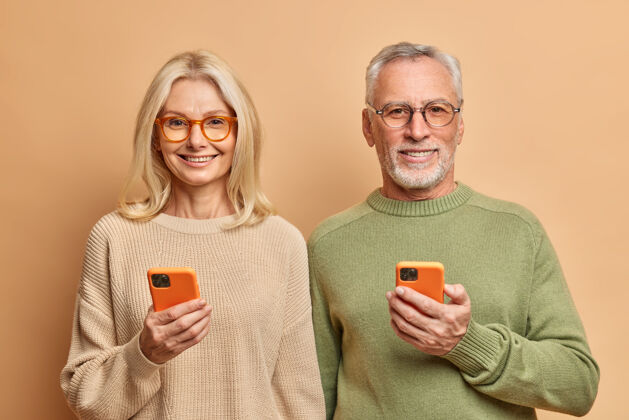 成熟人的年龄和科技观念中年男女手持智能手机的写真 短信男性满意